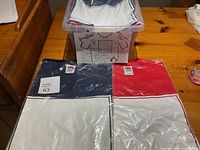 12 Fruit of the Loom graphic T-shirts packaged in plastic, visible colors red and navy blue with white, stacked in a plastic bin and individually.
