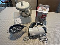 Photo showing all four appliances together on a table: Sunbeam hand mixer with beaters, vintage food processor, plastic jug strainer, and Amco Houseworks grater box