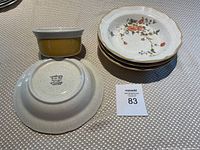 Stack of four floral design bowls alongside one yellow ramekin, set on a woven textured table surface, showing bottom stamp of Mikasa Garden Club Joy.