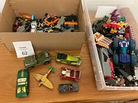 Mixed toy vehicles and action figures in box and bins, showing variety of items including die-cast cars, trucks, and Transformers figures.