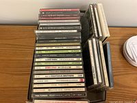 Photo showing stacked music CD jewel cases with artist names and album titles visible including Elton John, George Strait, Buddy Holly, Tina Turner, Kenny Rogers