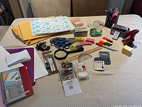 Entire assortment of over 30 mixed office supplies arranged on table including scissors, stapler, stamps, markers, envelopes, clips, push pins, notebooks and papers.