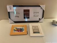 Set of five picture frames displayed on a table, showcasing various sizes and materials including wood and plastic. Large black frame with three slots and three smaller frames in white and natural wood finishes.