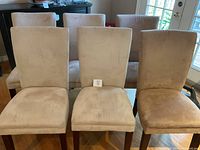Front view of six upholstered dining chairs in two shades of beige/taupe microfiber fabric, showing wood legs and padded seats and backs