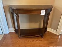Full view of the dark brown wooden demilune console table showing traditional styling and curved half-moon top with lower shelf.