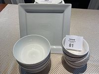 Photo of set showing large smooth white bowls stacked, smaller textured white bowls stacked, and large square white plate in background.