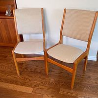 Front view of two teak dining chairs showing upholstery and wood frame