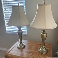 Both matching brass-tone table lamps with shades on wooden surface