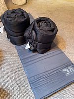 Two rolled black sleeping bags on top of grey underlay