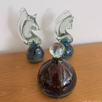 Three glass pieces on tabletop: two horse head sculptures and one bottle