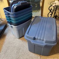 Stack of seven plastic totes with lids nested together beside single tote