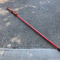 Full view of red pole pruner lying on ground