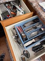 Two kitchen drawers open showing flatware tray and utensil drawer