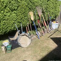 Wide view of long-handle garden tools lined against hedge with pop-up bin
