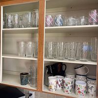 Cabinet with assorted clear glasses and printed ceramic mugs