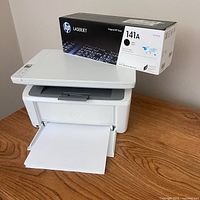 Printer front with paper tray extended and HP 141A toner box on top