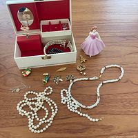 Overview of jewelry box open with contents and assortment of costume jewellery laid out