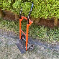 Full view of orange and black convertible hand truck standing upright on lawn