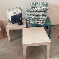 Overall lot showing two beige tables, green table, cooler, travel mug, stack of cushions