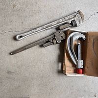Three plumbing tools laid out: two pipe wrenches and pipe cutter