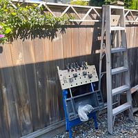Overall view of aluminum ladder beside blue metal sawhorse workbench with clamps attached