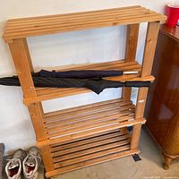 Full view of wooden shoe rack with two umbrellas resting on shelves