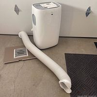 Portable AC unit with hose and window panel on floor