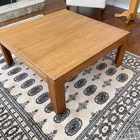 Full view of square teak coffee table on rug