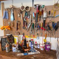 Pegboard with assorted hand tools hanging and supplies on bench