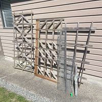 Three trellises and three chicken-wire rolls leaning against exterior wall