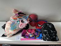 Overview of accessories including Easter ears headbands, Spider-Man masks and costume, butterfly wings with wand and crown, Moana necklace, Addams Family Wednesday dress and wig.