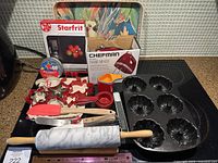Photo of baking items including Starfrit kitchen scales box, Chefman hand mixer box, assorted cookie cutters, measuring cups and spoon, marble rolling pin, Nordic Ware Bundt muffin tray, cake making utensils and a Cockatoo kitchen tray with visible damage.