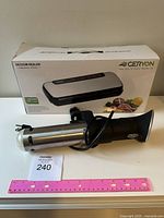 Photo of sous vide immersion cooker placed next to a pink ruler showing length, with Geryon vacuum sealer box in background