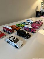 Front angle of assorted children's toy cars showing various colors including red, pink, green, black, and white cars.