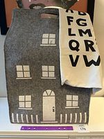 Large dark gray house-shaped felt storage bag with white printed windows, door, and railing, showing front face with cutout handles