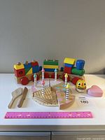 Photo of all wooden toys including birthday cake with candles, two small rattles, and wooden stacking train set with ruler for scale