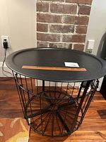 Full view of black round metal coffee table with wireframe base and removable lid on top, showing tray surface and storage space inside base.