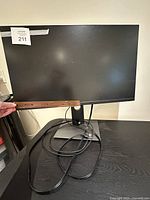 Dell computer monitor front view with cables and adjustable stand on black table.