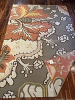 Full view of Pier 1 Imports large area rug with floral and geometric pattern in multiple colors including orange, gray, pink, cream and yellow on hardwood floor.