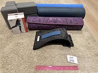 Yoga mats rolled, yoga blocks with bite marks, boxed New Balance stretch bands, black neck stretch device on carpeted floor.