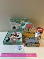 Assorted children's games displayed, includes boxed Little Cooperation, Scoops Meow stacking game, tins of memory games, and puzzle packaging.