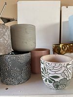 Group of assorted indoor plant pots of varying colors, including grey floral embossed, beige and pinkish brown plain pots, white with floral pattern.