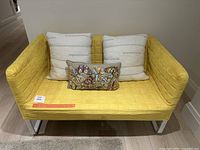 Full view of yellow Ikea Knopparp loveseat with two large white cushions and one rectangular decorative cushion with butterfly embroidery.