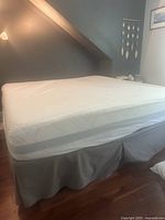Assembled king mattress on grey upholstered base with valance sheet in room