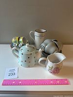 Front view of the teapot, milk jugs, cups, saucers, and Mini Bluey espresso cups with saucers arranged on a white surface with a pink ruler for scale.