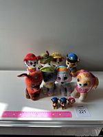Front view showing the 8 plush Paw Patrol characters lined side by side, with ruler and lot number in front