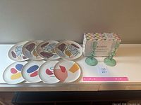 Photo showing set of 8 bamboo plates arranged on table with green glass candlestick pair boxed, pink ruler for scale