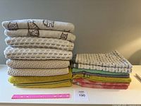 Two stacks of bath and hand towels in various colors and textures on a surface with a pink ruler in front to show size.