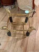 Oblique view showing brass frame, black ribbed leg accents, and tempered glass top