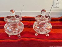 Both crystal condiment pots with lids and spoons on display